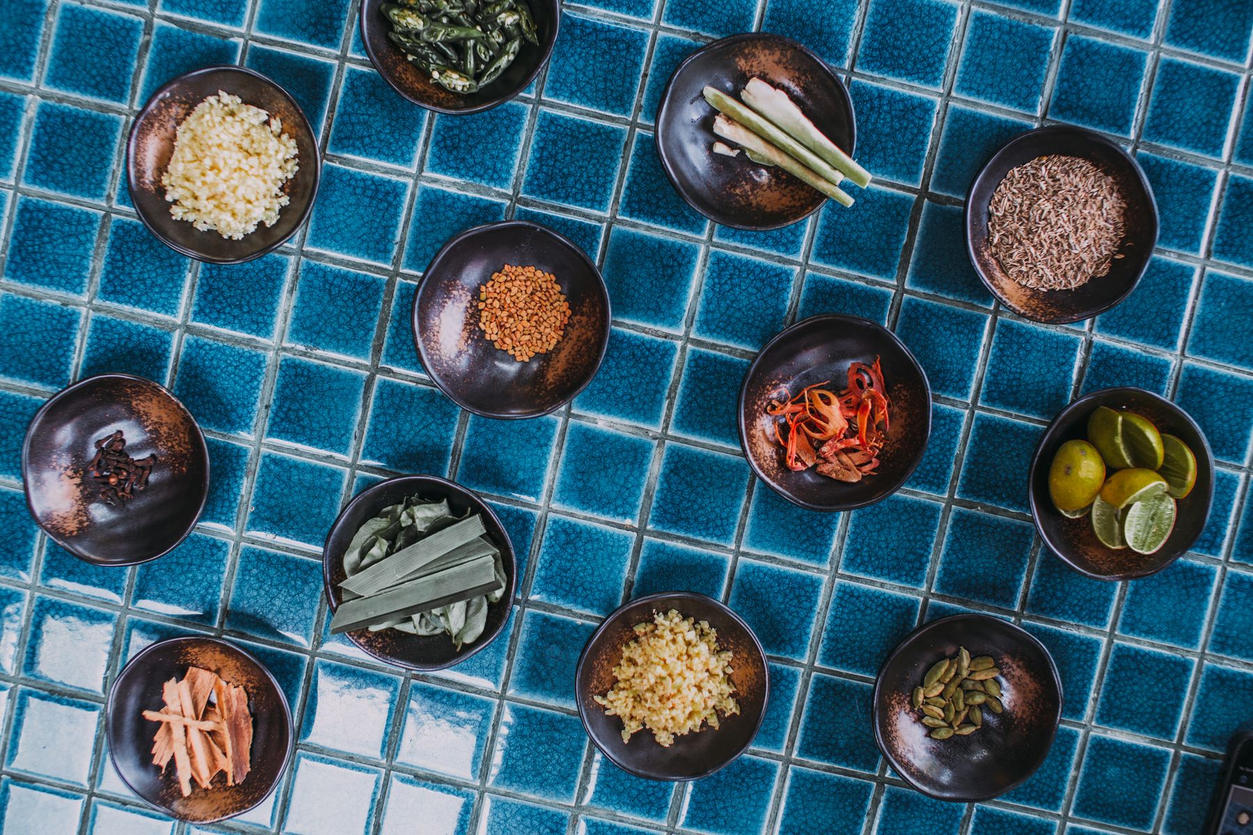 An overhead arrangement of culinary herbs, spices, and ingredients in bowls