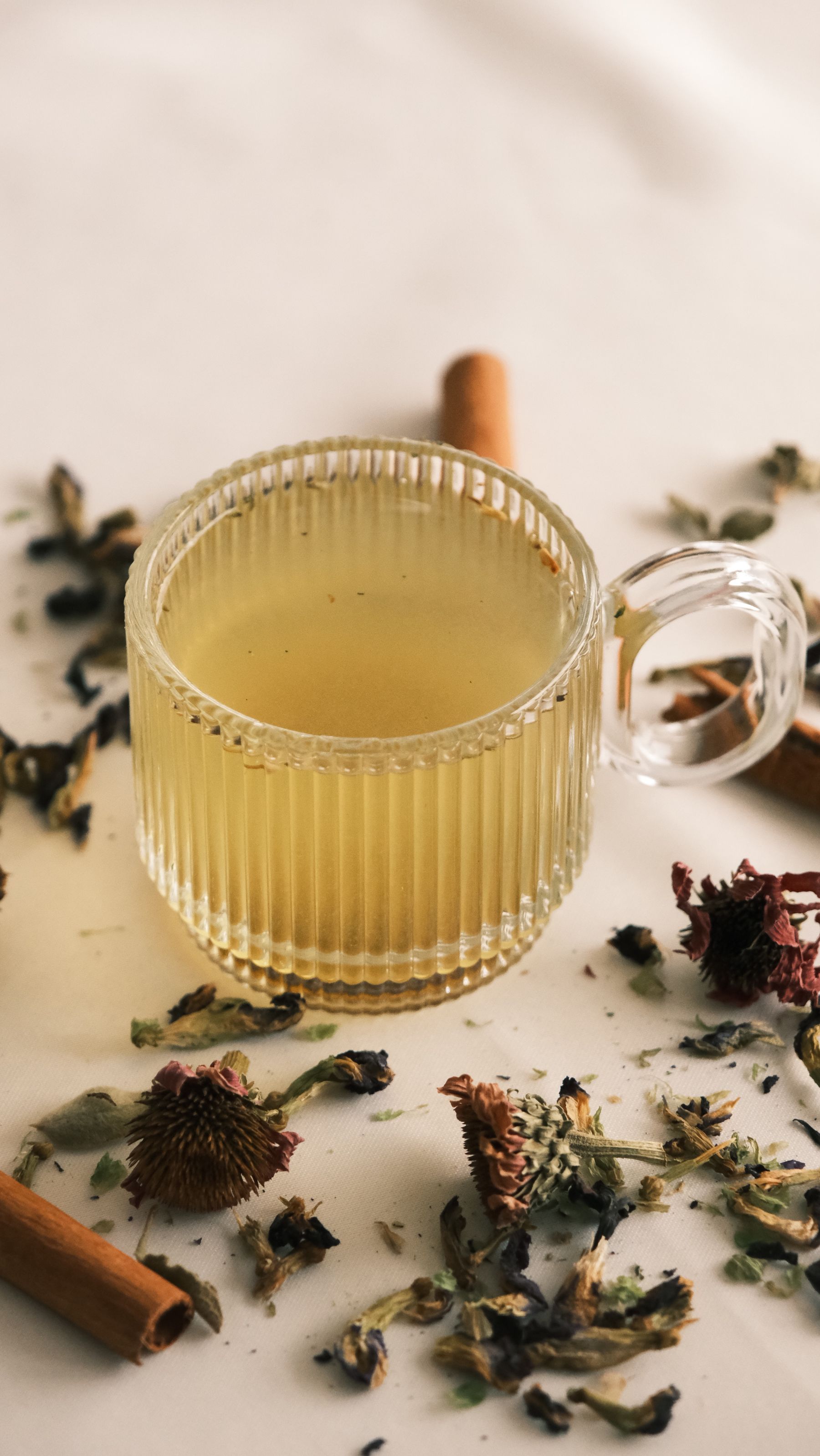 A glass cup of herbal tea with dried flowers and cinnamon